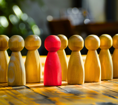 Conversion to Hire Rows of wooden peg figures with one red piece centered among yellow ones, standing out on a sunlit wooden table.