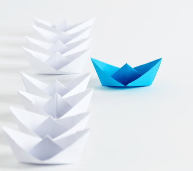 Conversion to Hire Row of white paper boats in soft focus with a single bright blue origami boat set apart in front on a white surface.