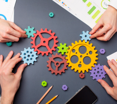 Discovery & Consultation Hands arrange colorful gear cutouts on a desk with charts and a phone, illustrating teamwork and process integration.