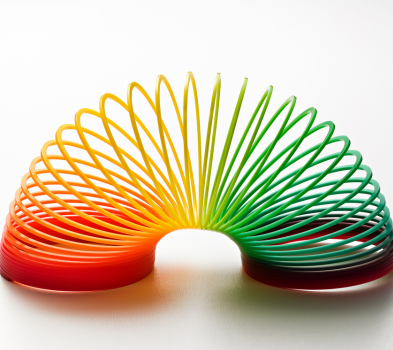 Flexible and Fast Rainbow-colored plastic slinky toy arched in a curve, shifting from red and orange to yellow, green, and teal.