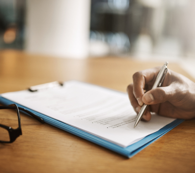 Offer & Onboarding Two men in business attire smiling as one hands a document to the other in a modern office setting.
